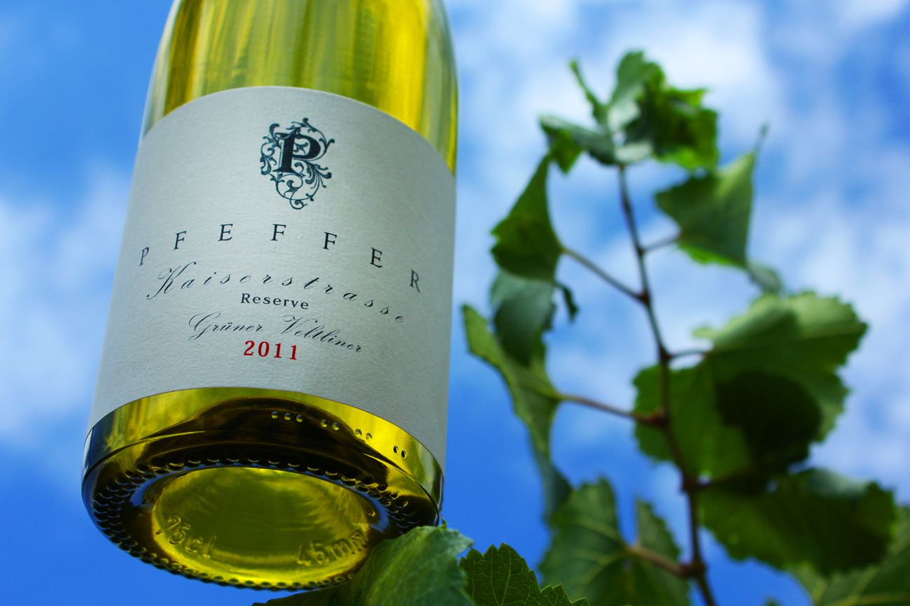 Láhev vína s etiketou "Pfeffer Kaiserstrasse Reserve veltlínské zelené 2011" na pozadí modré oblohy a vinných listů.