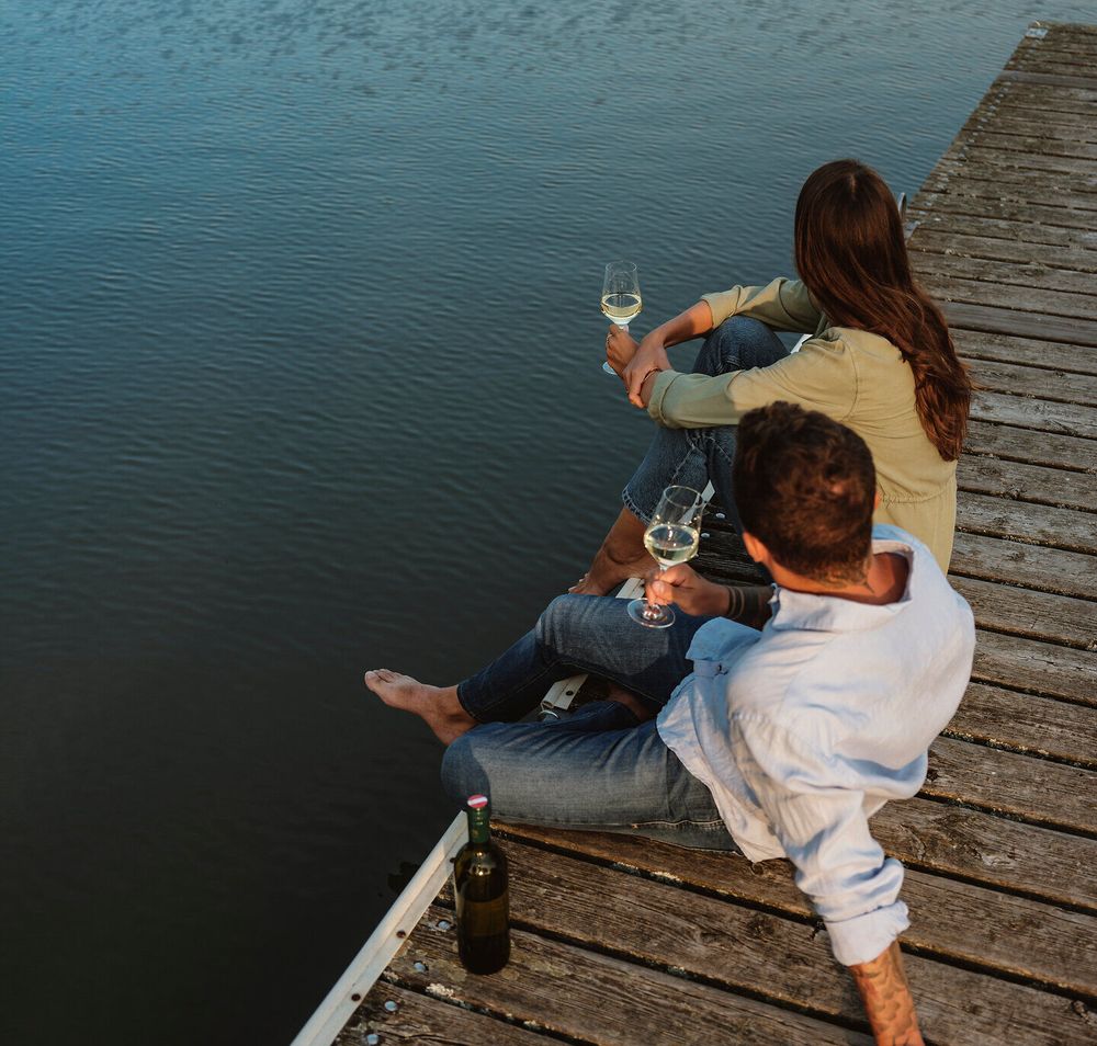 Am Ufer des malerischen Landschaftsteichs genießen zwei Personen eine entspannte Auszeit. Mit einem Glas Wein in der Hand blicken sie auf die ruhige Wasseroberfläche, während die sanfte Brise die Atmosphäre erfrischt. Diese friedliche Kulisse lädt dazu ein, die Schönheit der Natur in vollen Zügen zu erleben.