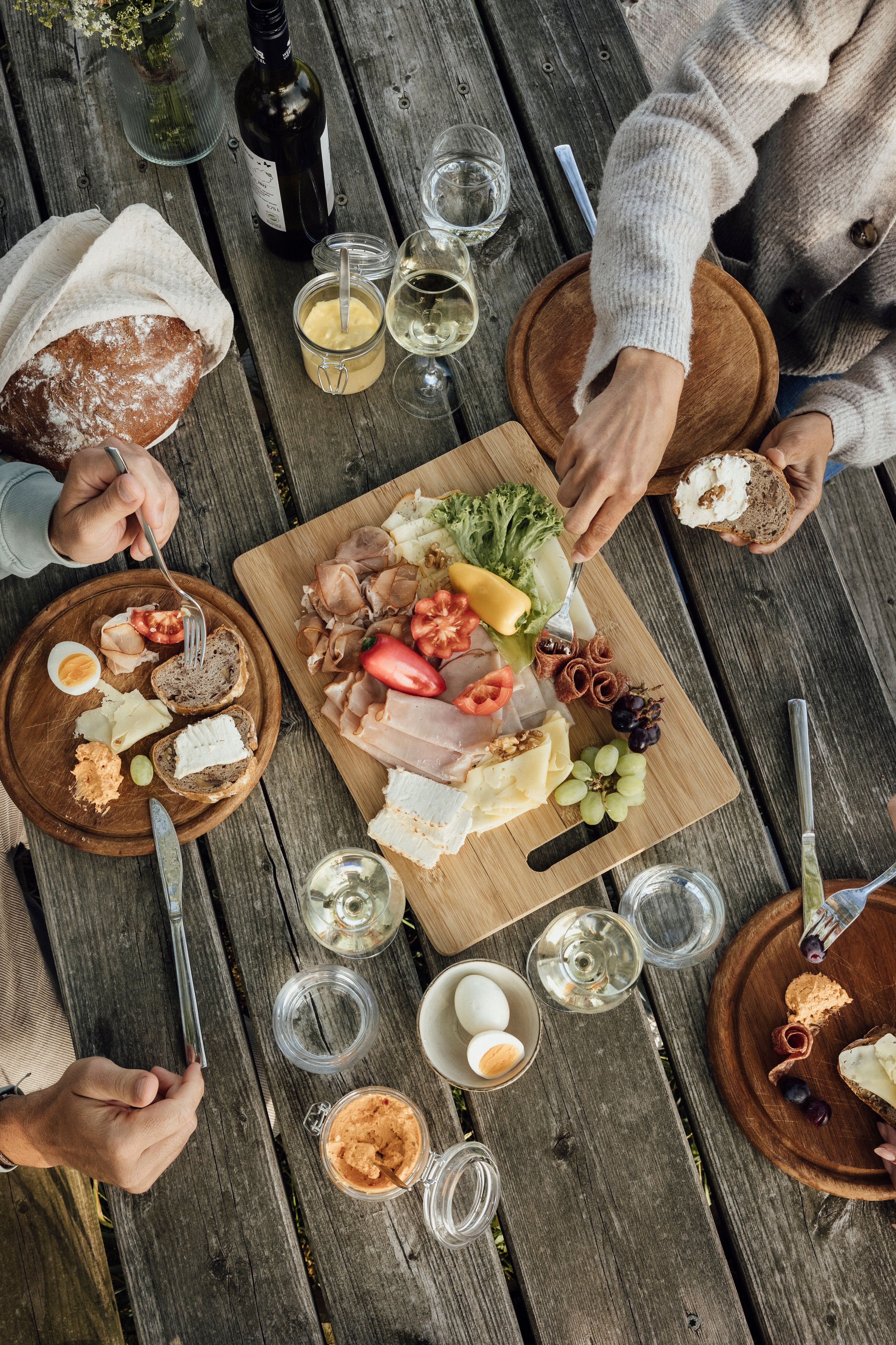 Ein rustikaler Holztisch mit einer Jause aus Brot, Käse, Wurst, Gemüse und Wein.