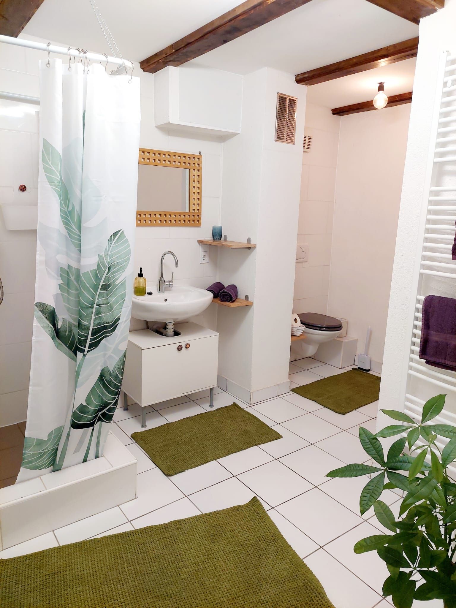Modernes Badezimmer mit weißen Fliesen, grünen Teppichen und Pflanzenmotiv-Duschvorhang.