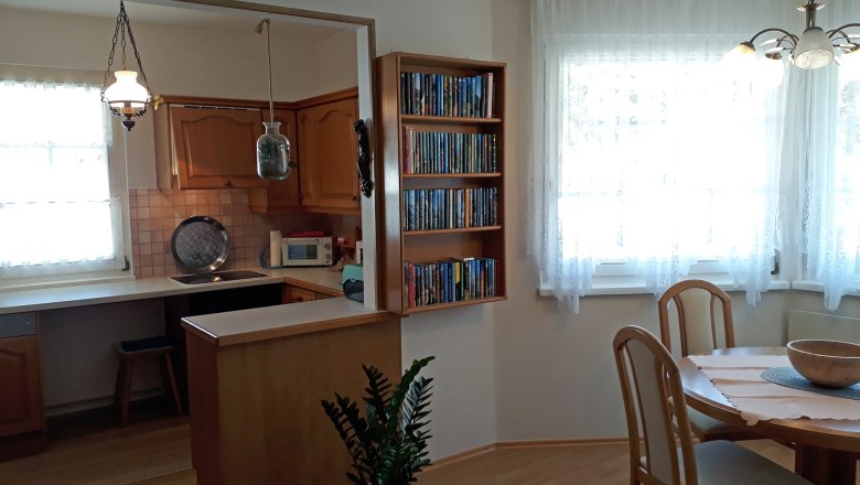 Gemütliche Küche mit Holzmöbeln, Esstisch und Bücherregal.