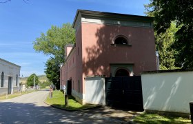 Stra&szlig;e mit rosa Geb&auml;ude und B&auml;umen bei sonnigem Wetter.
