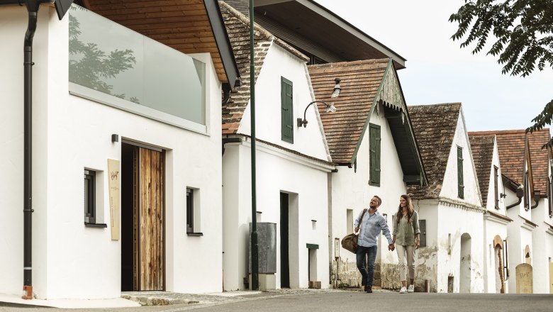 Ein Paar spaziert an traditionellen Weinkellern vorbei.
