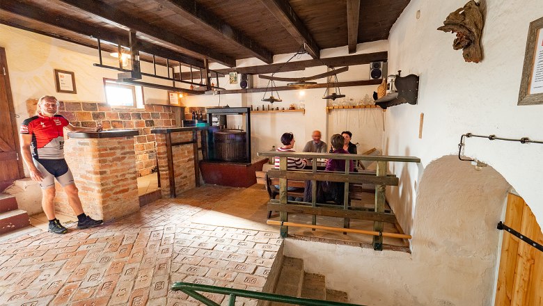 Gemütlicher Weinkeller mit Personen an einem Tisch und einem Mann in Radkleidung.