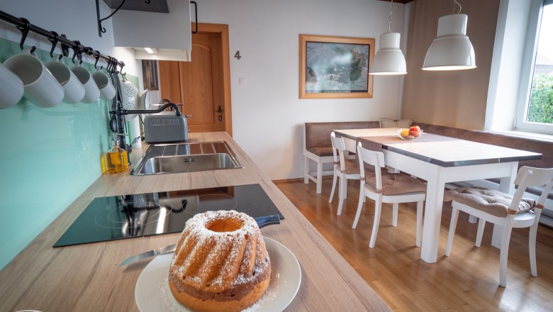 Moderne Wohnküche mit Esstisch, Stühlen und Gugelhupf auf der Arbeitsplatte.