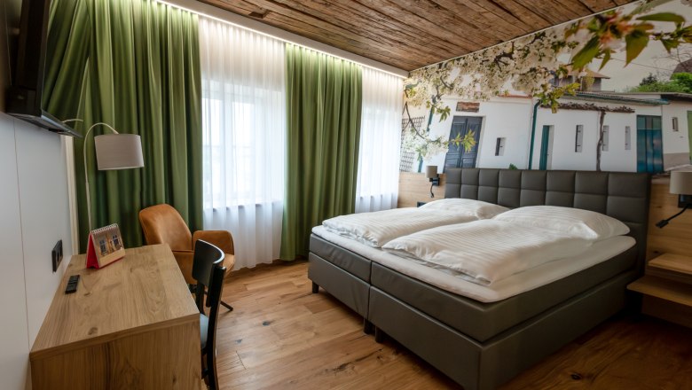 Modernes Gästezimmer mit Doppelbett, Holzboden und grünen Vorhängen.