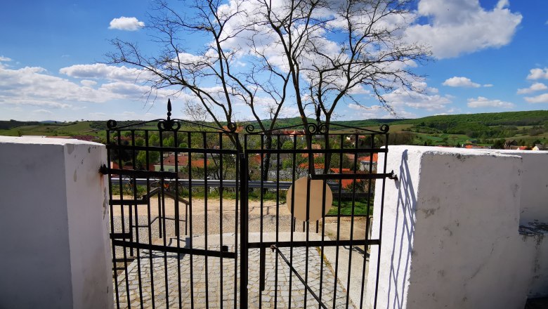 Friedhofstor aus Eisen mit Blick auf Landschaft und Dorf.