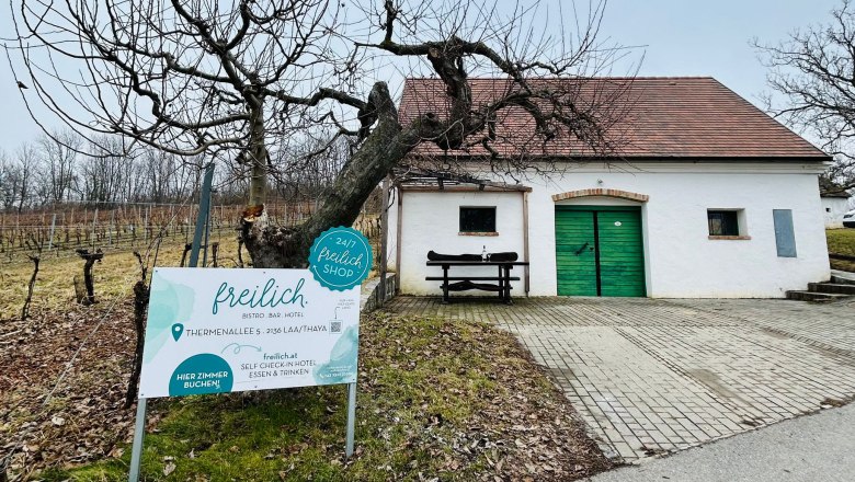 Wei&szlig;es Geb&auml;ude mit gr&uuml;nem Tor und Schild 'freilich' in einer l&auml;ndlichen Umgebung.