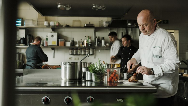 Köche arbeiten in einer professionellen Küche, einer schneidet Fleisch.