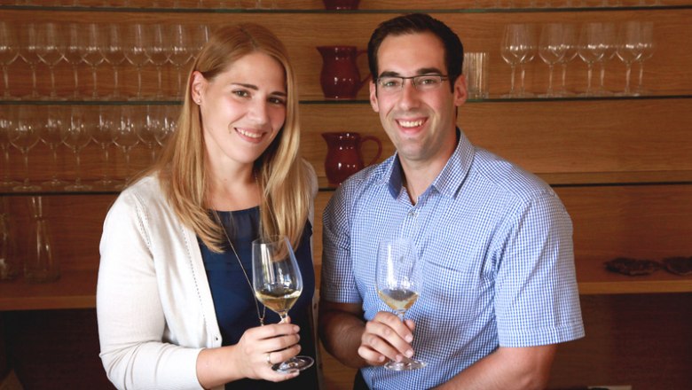 Ein l&auml;chelndes Paar h&auml;lt Weingl&auml;ser in einem Weinkeller.