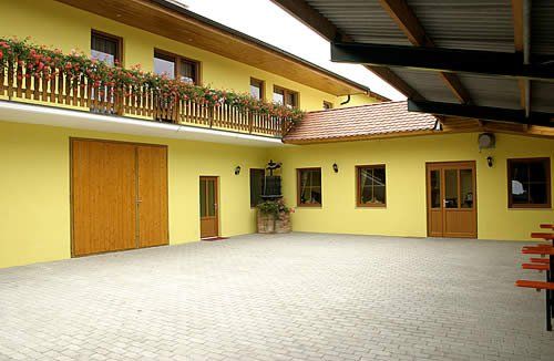 Innenhof eines gelben Gebäudes mit Holztüren und Balkon mit Blumen.