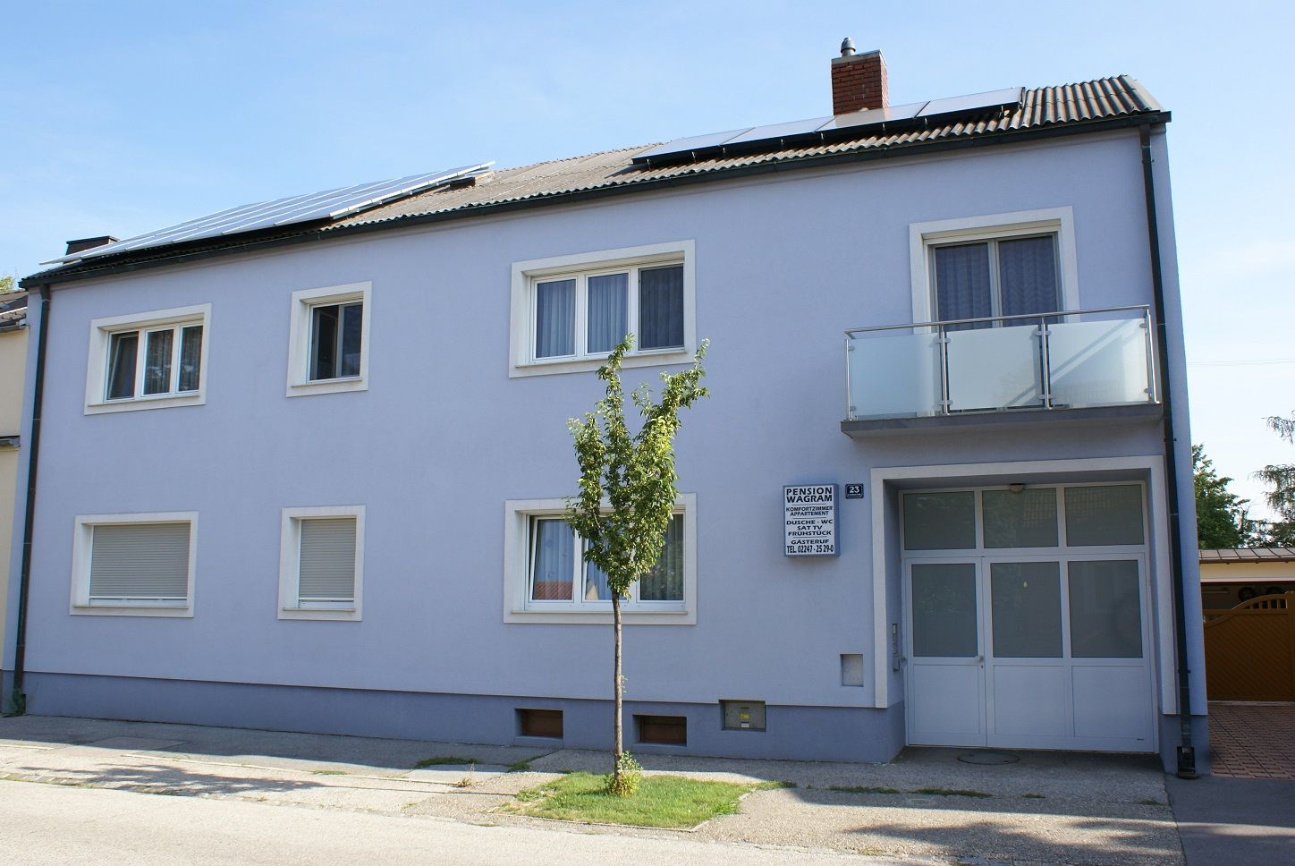 Vnější pohled na dvoupodlažní budovu s modrou fasádou a solárními panely na střeše.