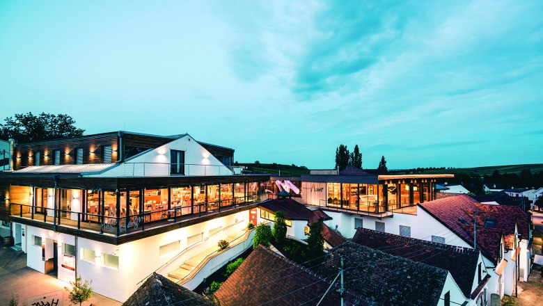 Modern winery architecture at dusk with illuminated interiors and surrounding buildings.