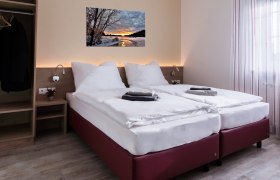 Modernes Doppelzimmer mit zwei Einzelbetten, Bild an der Wand, Kleiderschrank und Fenster mit Vorhängen.