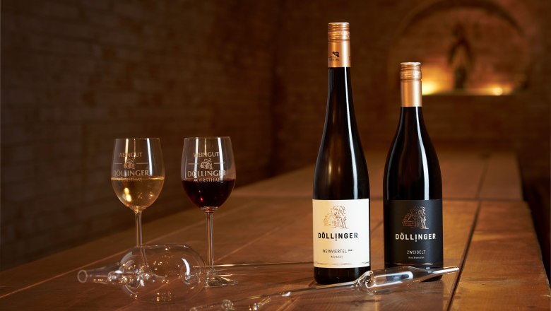 Zwei Weingl&auml;ser und zwei Weinflaschen auf einem Holztisch in einem Weinkeller.