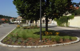 Ein gepflegtes Blumenbeet mit gelben Blumen und Bäumen in einer ruhigen Wohnstraße.