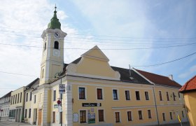 Gelbes Gebäude mit Turm und Uhr, Gasthaus zum schwarzen Adler, blauer Himmel.