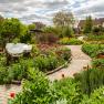 A well-tended garden with colorful flowers, a curved path and a tree stump with an information board.