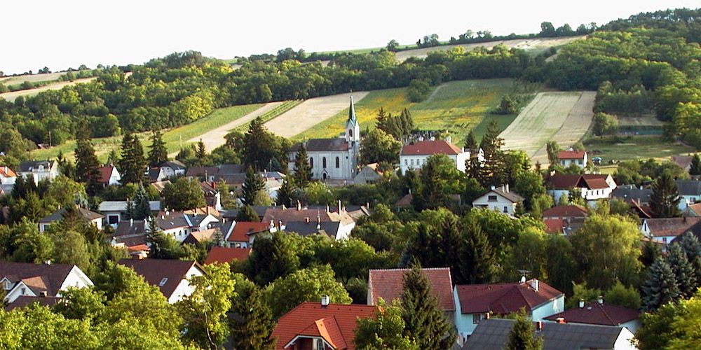 Landschaft mit Kirche und Dorf im Vordergrund, umgeben von Feldern und Hügeln.