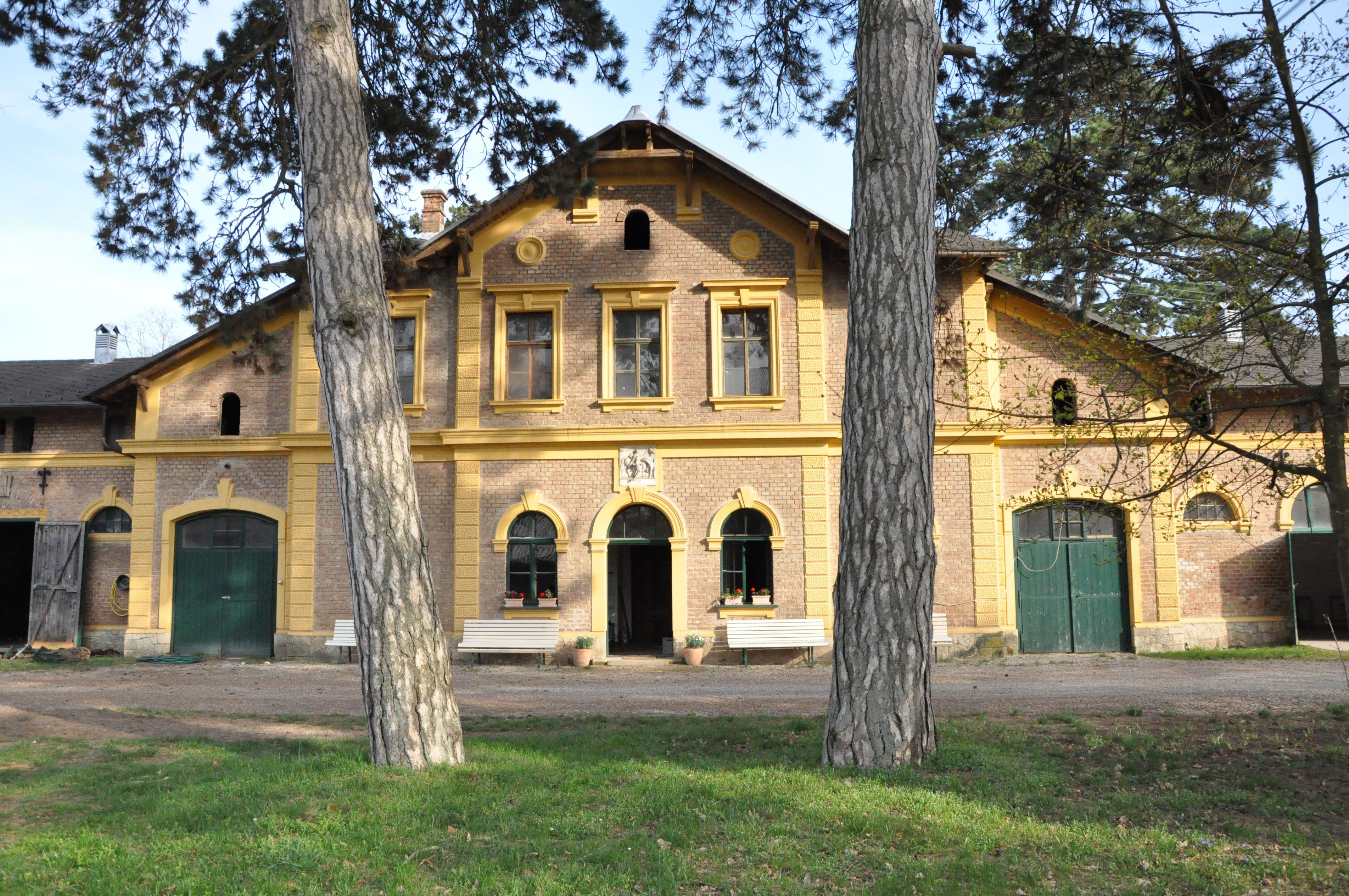 Historic building with yellow window frames and green doors, surrounded by trees.