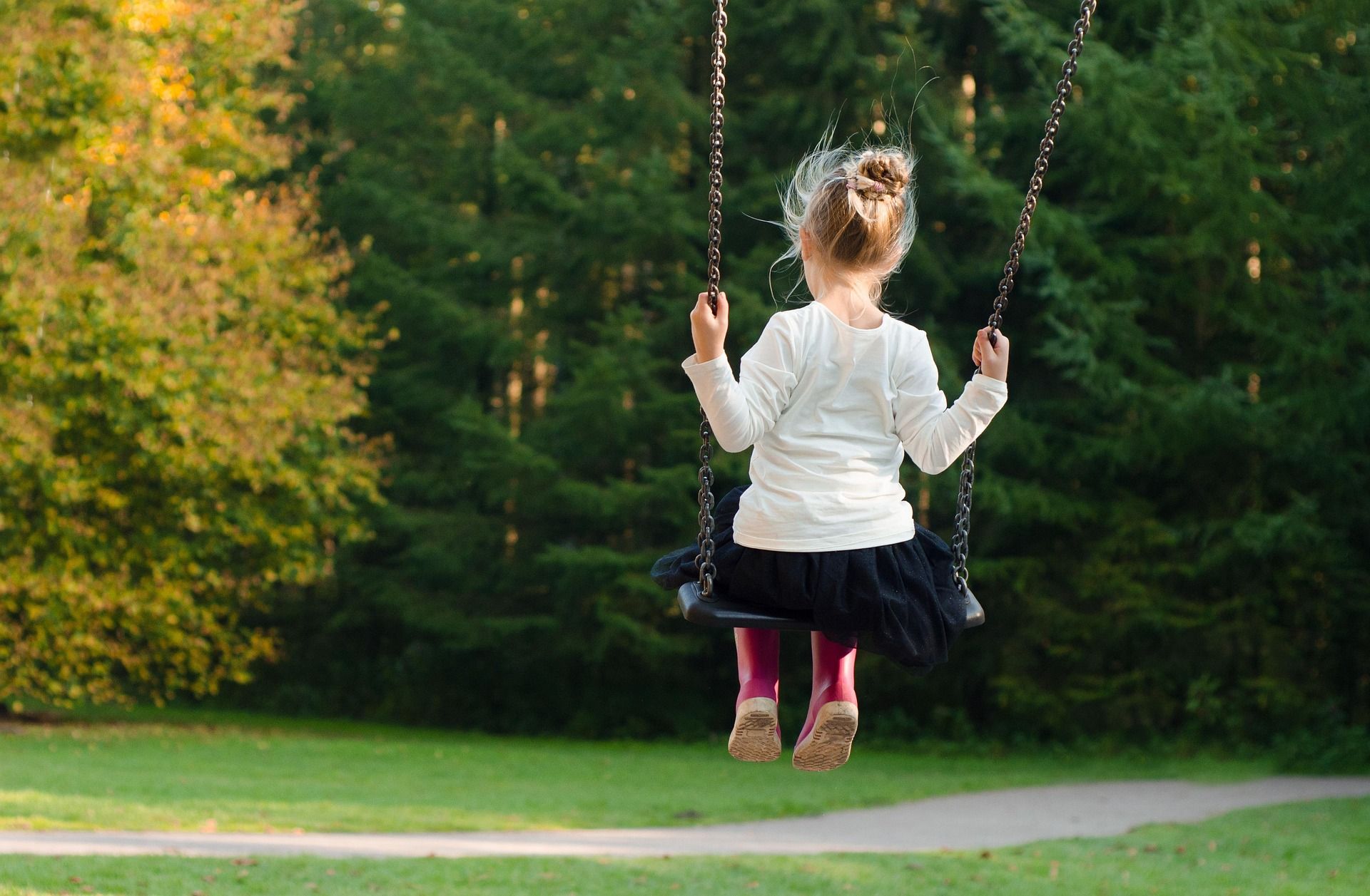 A child swings in a park surrounded by green trees.