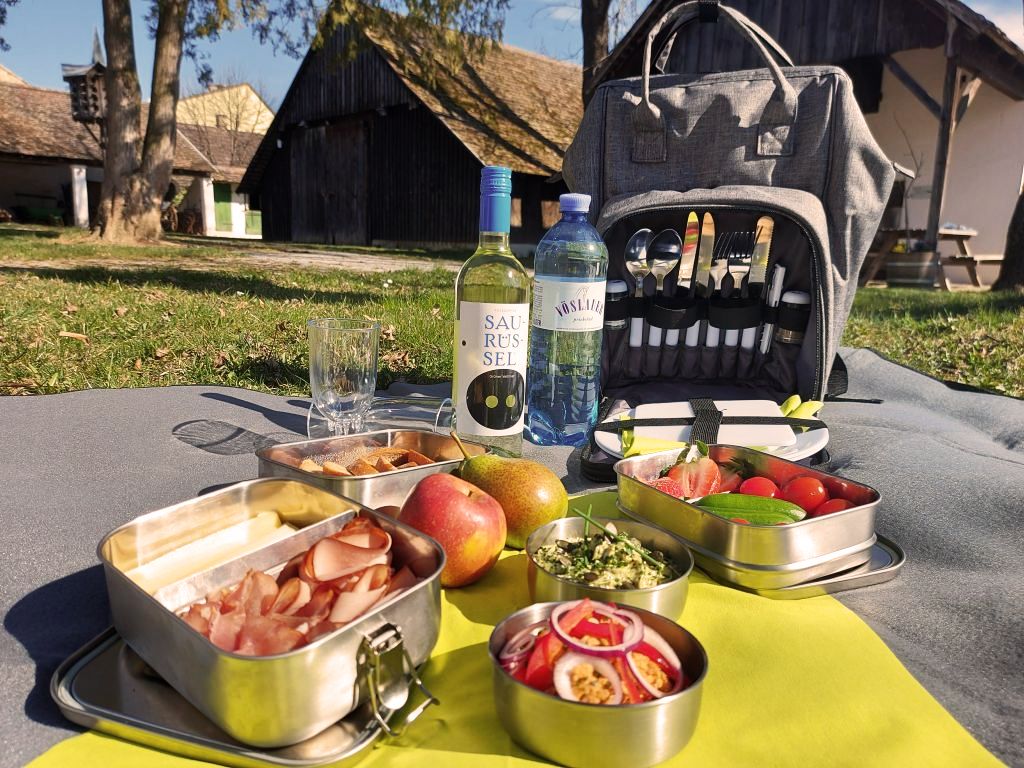 Auf einer Picknickdecke sind regionale Köstlichkeiten, eine Flasche Wein und Wasser ausgebreitet.