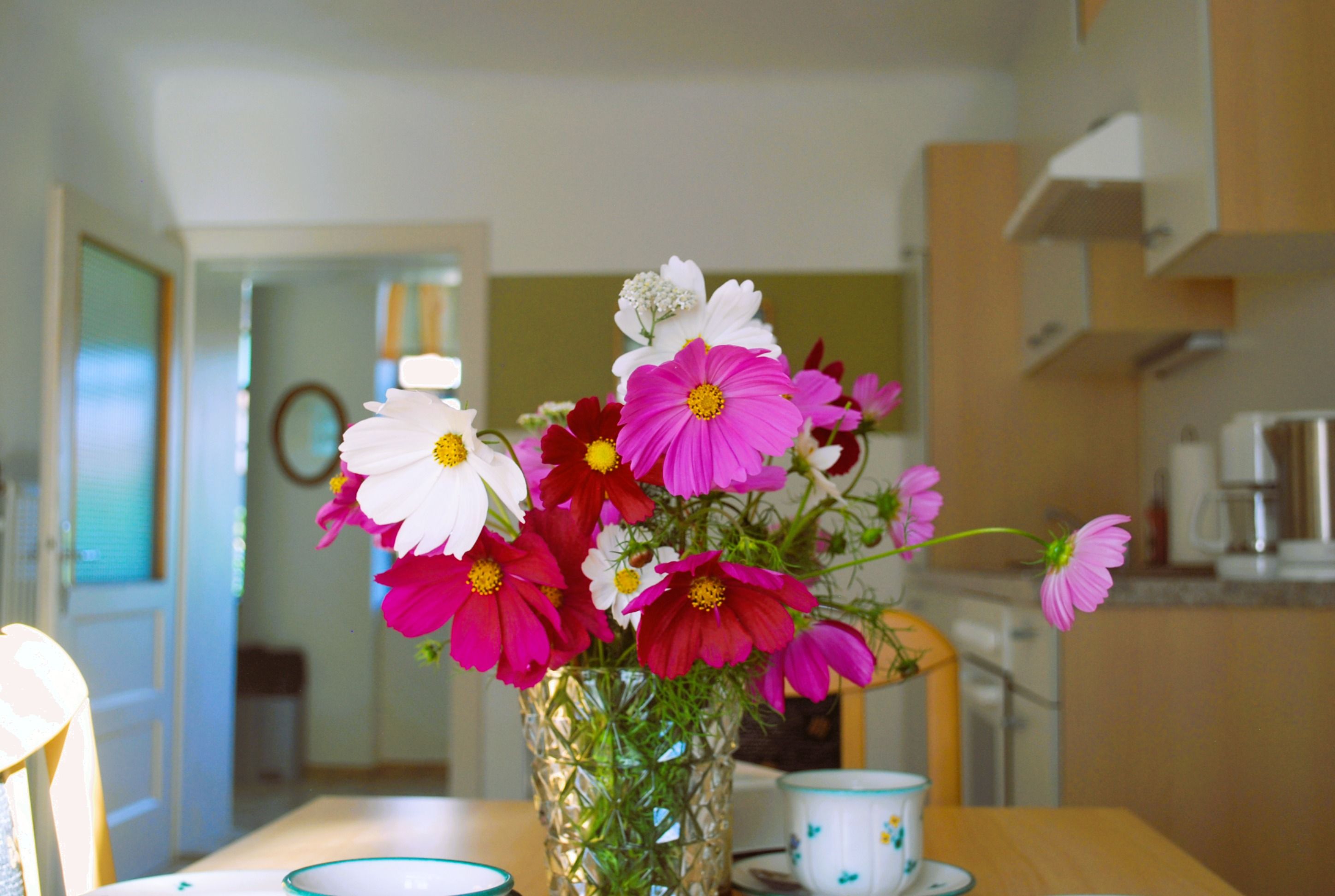 Ein Blumenstrauß mit rosa und weißen Blüten steht in einer Vase auf einem Tisch in einer Küche.
