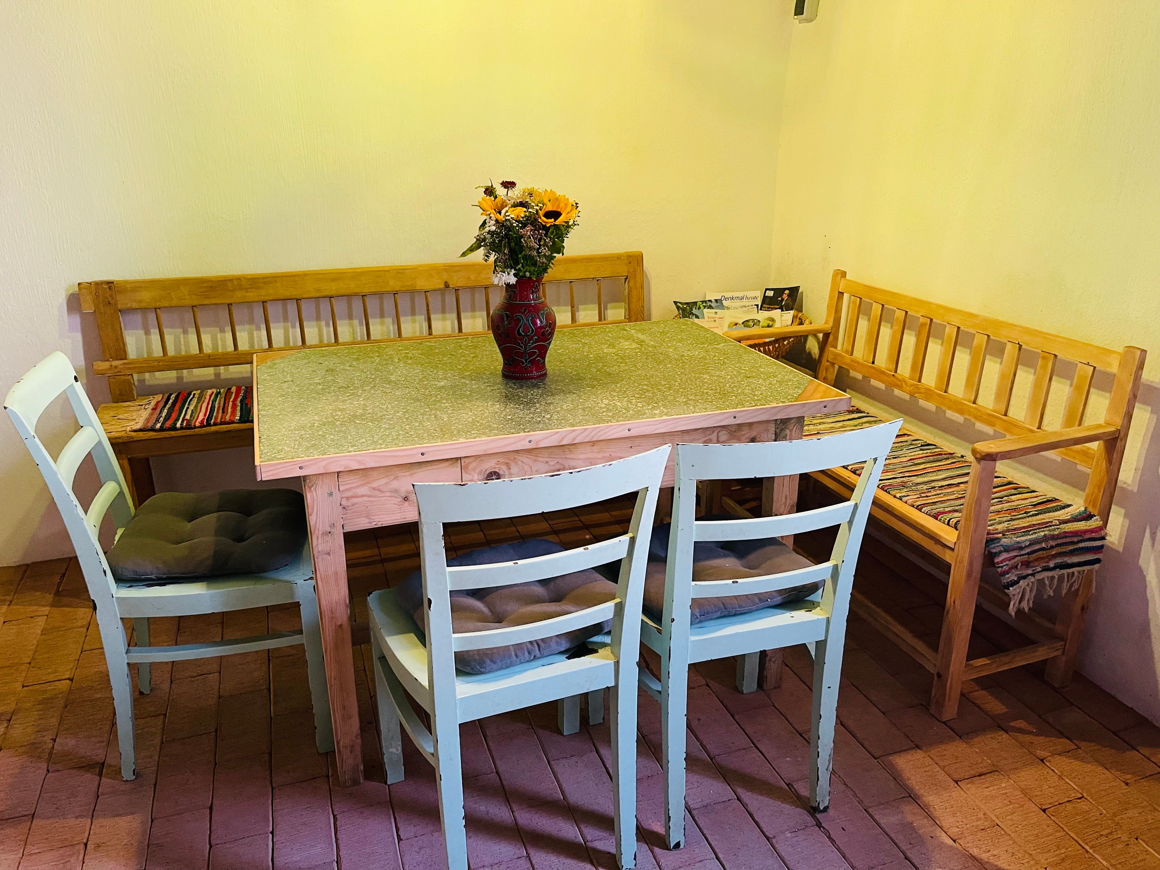 A cozy dining area with a wooden table, two chairs and two benches. There is a vase with sunflowers on the table.