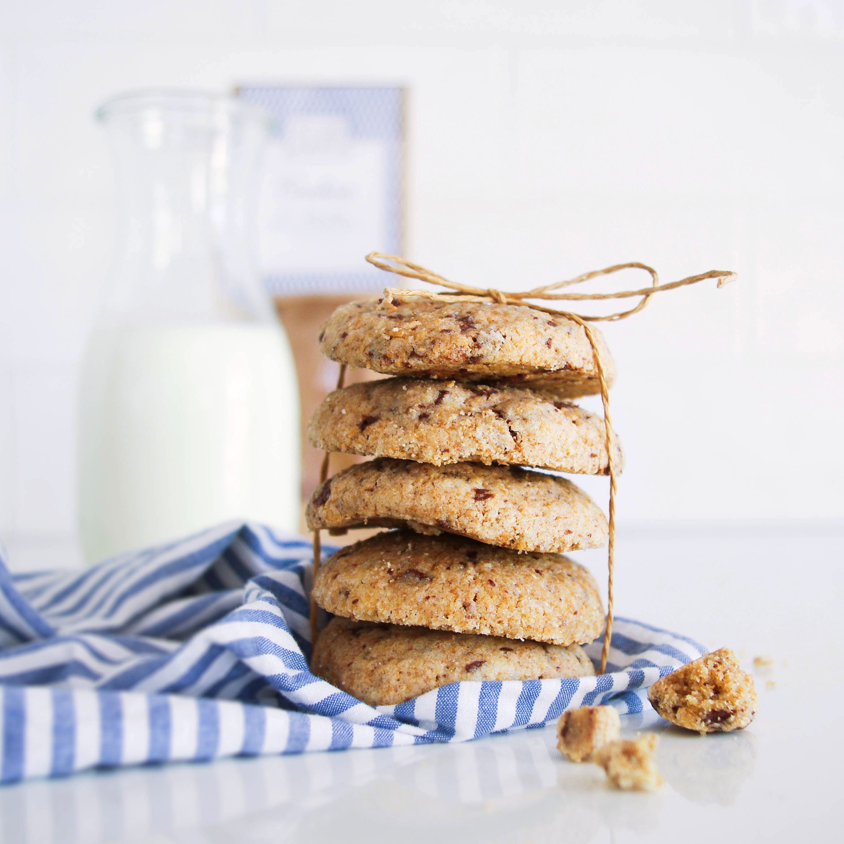 Ein Stapel von fünf Keksen, mit einer Schnur gebunden, steht auf einem blau-weiß gestreiften Tuch. Im Hintergrund ist eine Milchflasche zu sehen.