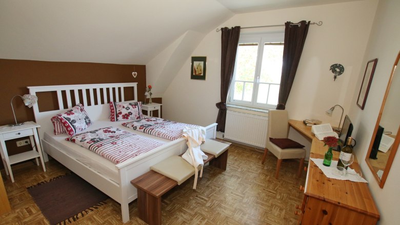 Gästezimmer, © Wolfgang Hanousek Gemütliches Gästezimmer mit Doppelbett, Sofa, Tisch und Stuhl. Braune Akzentwand und dunkle Vorhänge.