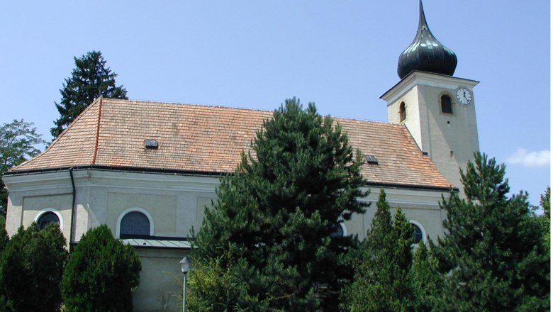 Kirche in Schleinbach mit Turm und Uhr, umgeben von B&auml;umen.