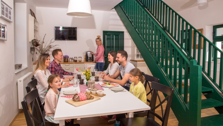 Familie sitzt an einem Tisch in einem modernen Esszimmer mit grüner Treppe.