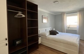 Modernes Schlafzimmer mit Doppelbett, Kleiderschrank und Fenster mit Vorhängen.