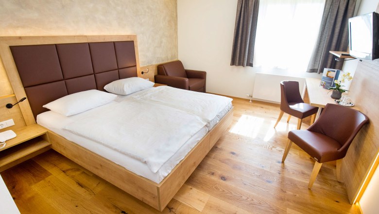 Modern eingerichtetes Hotelzimmer mit Doppelbett, Schreibtisch, Stühlen und einem Sessel.
