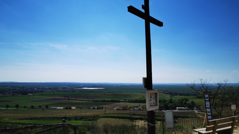 Ein gro&szlig;es Holzkreuz auf einem H&uuml;gel mit Blick auf eine weite Landschaft unter blauem Himmel.
