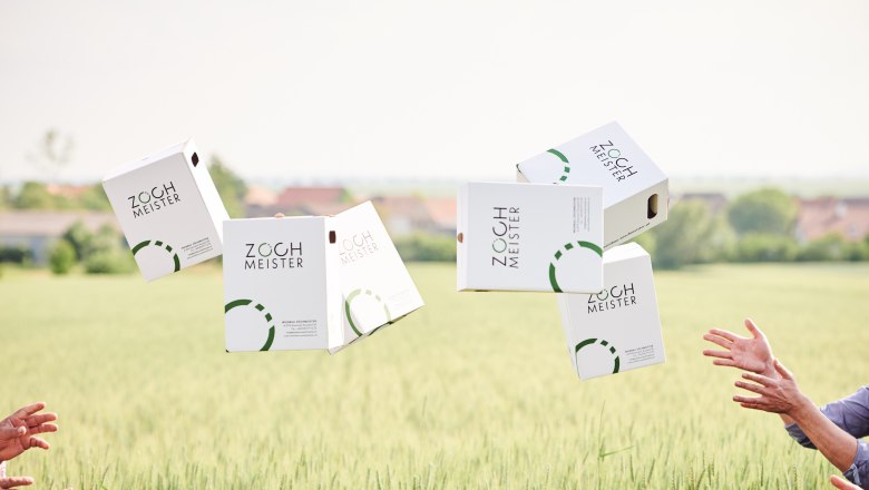 Weinkartons von Z&ouml;chmeister fliegen &uuml;ber ein Feld, H&auml;nde fangen sie.