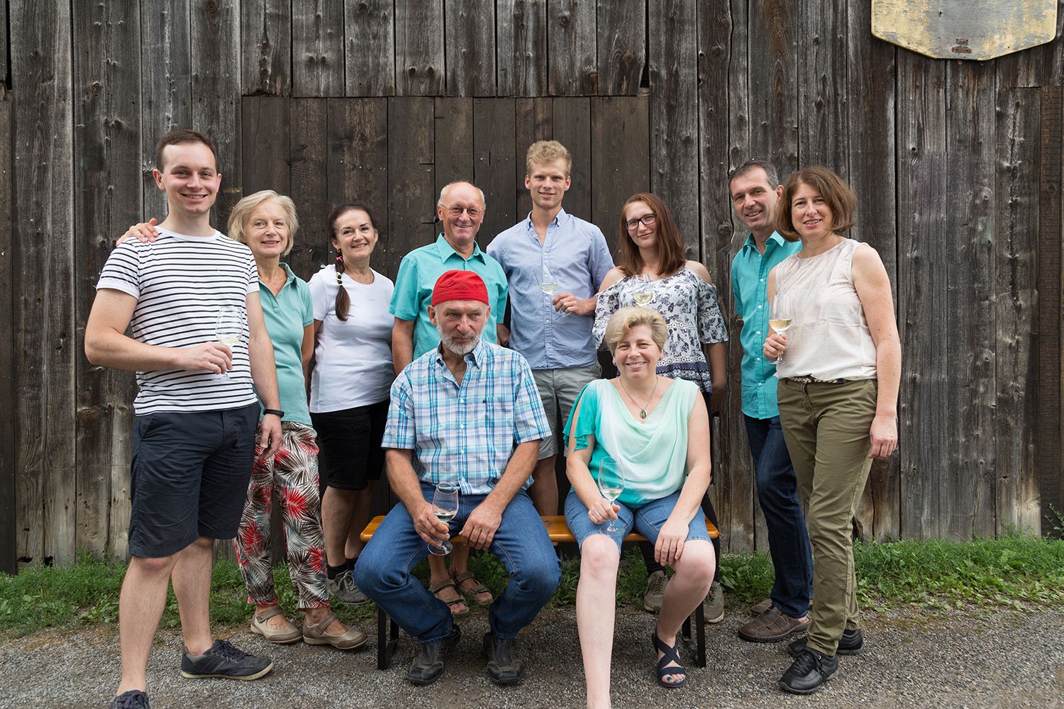 A group of ten people pose smiling in front of a wooden wall, some holding wine glasses.