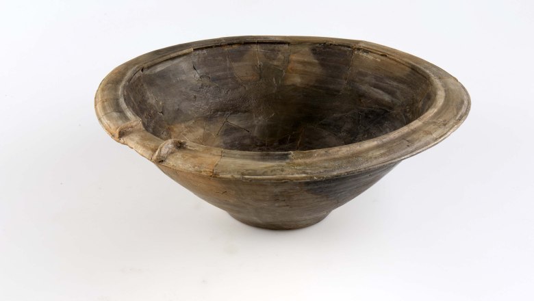 An antique, brown clay bowl with a wide rim and visible cracks on a white background.