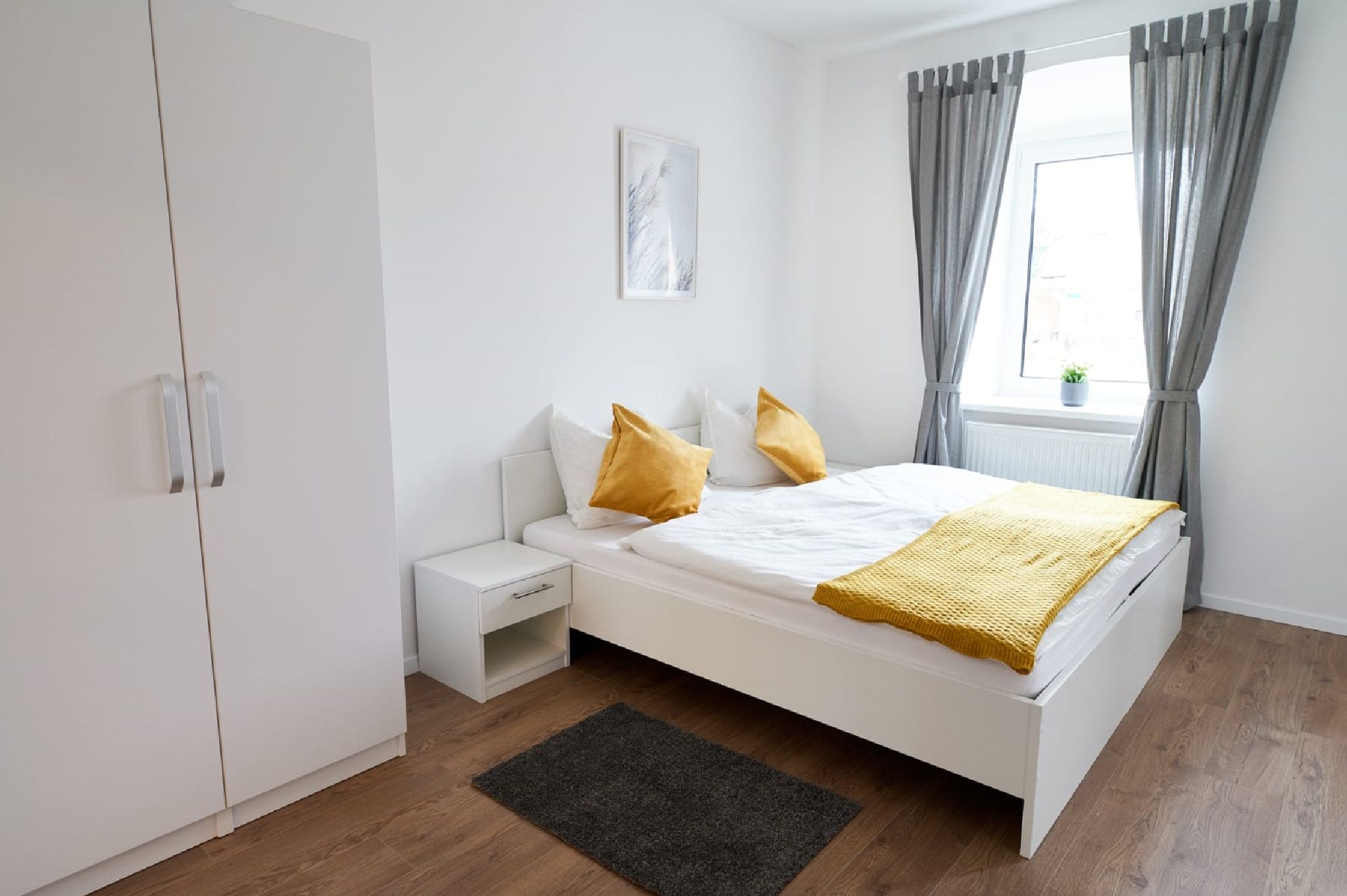 Modernes Doppelzimmer mit weißem Bett, gelben Kissen und grauen Vorhängen.