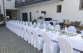 Langer, festlich gedeckter Tisch im Freien mit weißen Tischdecken und Stuhlhussen.