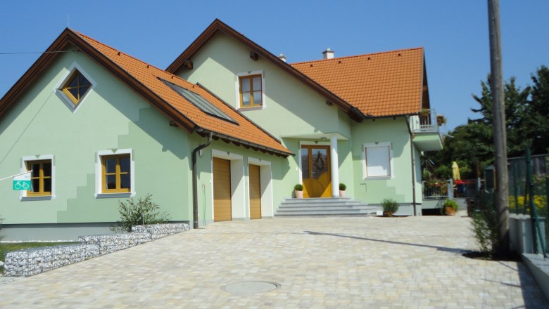 Ein modernes, zweistöckiges Haus mit grünem Anstrich und roten Dachziegeln, umgeben von einem gepflasterten Hof.