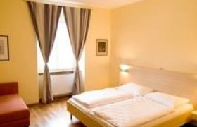 Ein gemütliches Doppelzimmer mit einem großen Bett, Holzboden, einem Sessel und einem Fenster mit Vorhängen.