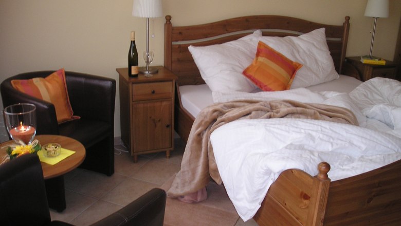 Gemütliches Gästezimmer mit Doppelbett, Nachttisch, Lampe, Sessel und Tisch.