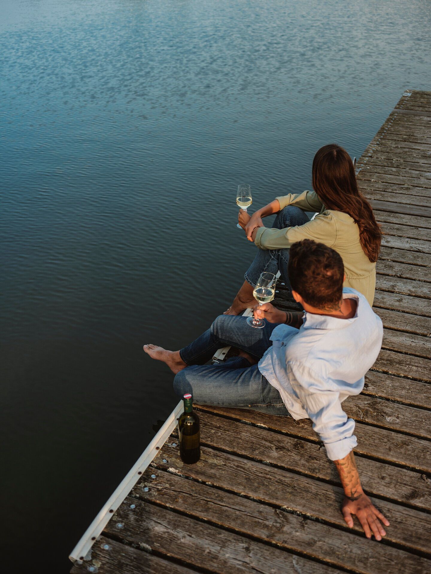 Am Ufer des malerischen Landschaftsteichs genießen zwei Personen eine entspannte Auszeit. Mit einem Glas Wein in der Hand blicken sie auf die ruhige Wasseroberfläche, während die sanfte Brise die Atmosphäre erfrischt. Diese friedliche Kulisse lädt dazu ein, die Schönheit der Natur in vollen Zügen zu erleben.