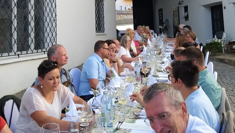 Eine lange Tafel mit Menschen, die im Freien speisen.