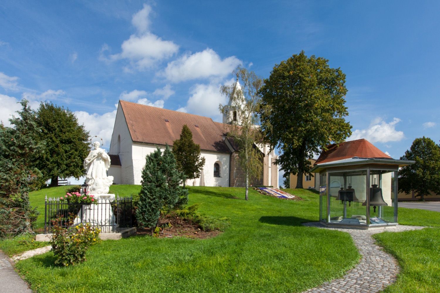Kirche in Großkrut mit Statue und Glockenhäuschen im Vordergrund.