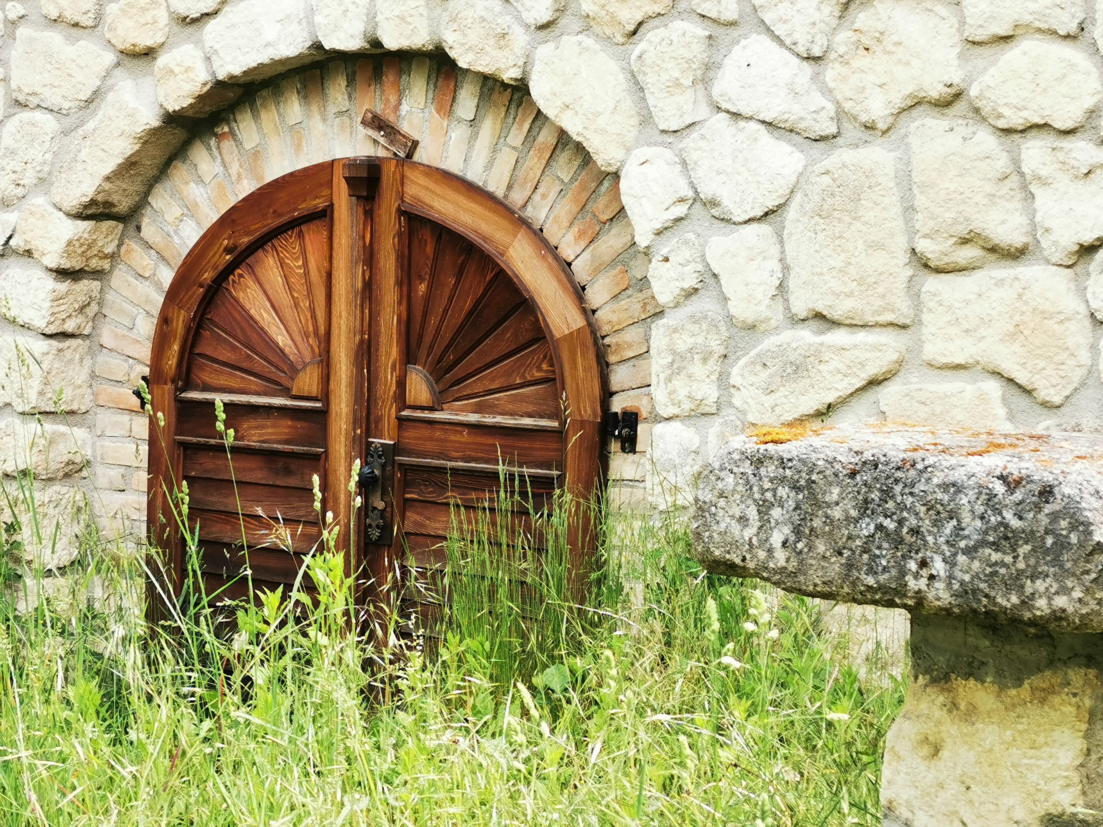 Holztür in Steinmauer mit Gras im Vordergrund.