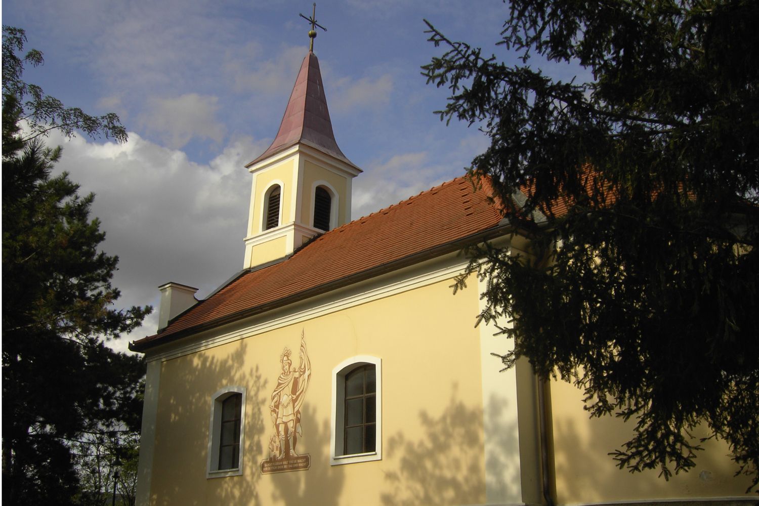 Florianikapelle Oberrohrbach mit Turm und Wandbild, umgeben von Bäumen.