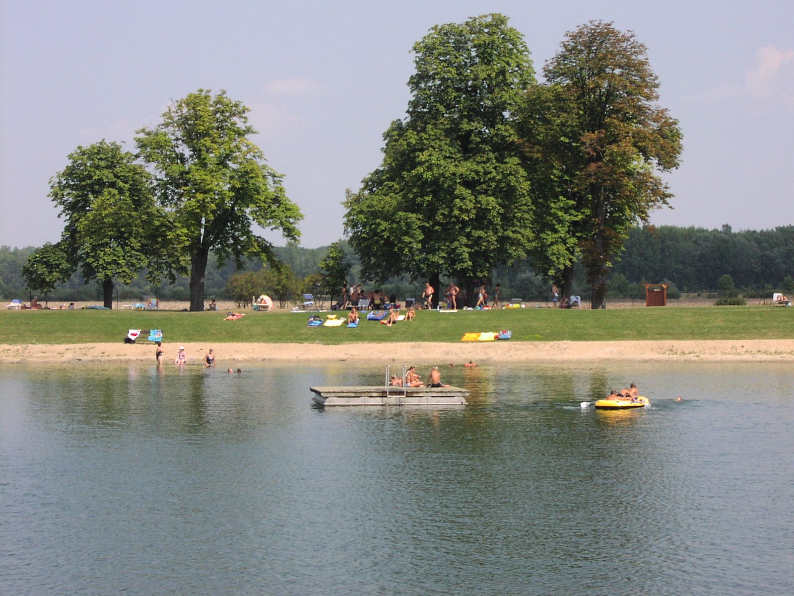 Menschen entspannen an einem See mit Bäumen im Hintergrund.