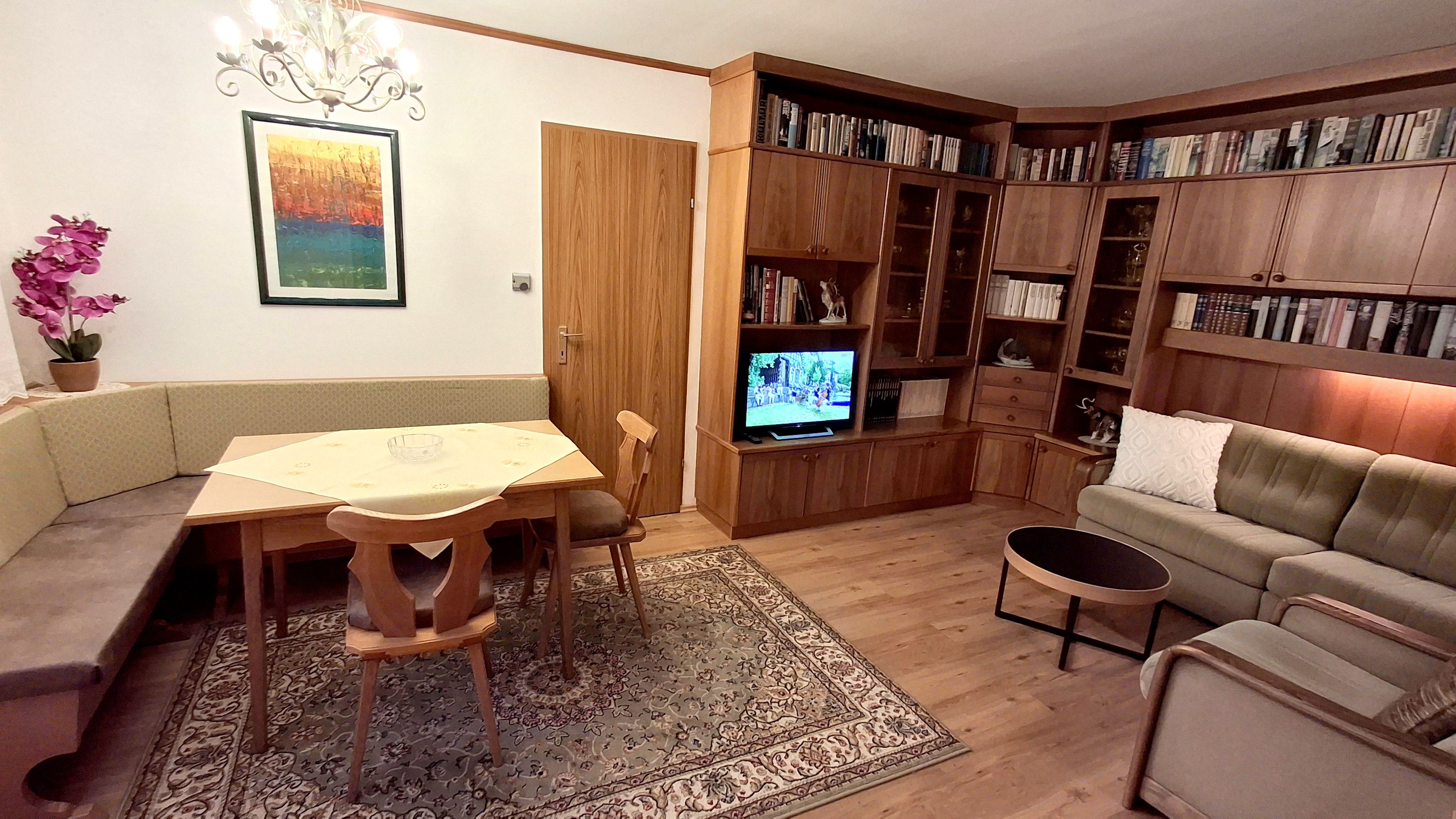 Útulný obývací priestor s rohovou lavicou, dreveným nábytkom, kobercom a TV.